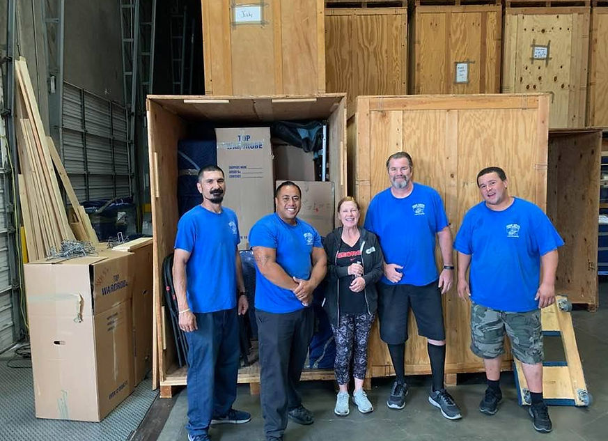 Group of Movers in Blue Shirts Five individuals in blue shirts standing in front of a large wooden crate in a warehouse.