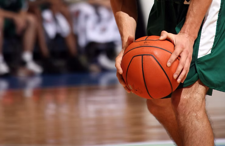 Close-up of a basketball player in green shorts holding a basketball during a game on a wooden court.