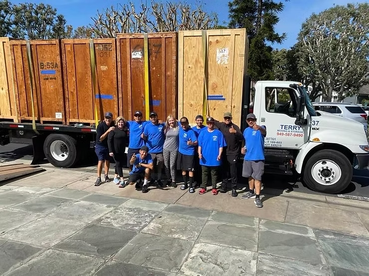 Group of movers and clients posing in front of a Terry Moving truck loaded with large wooden crates.