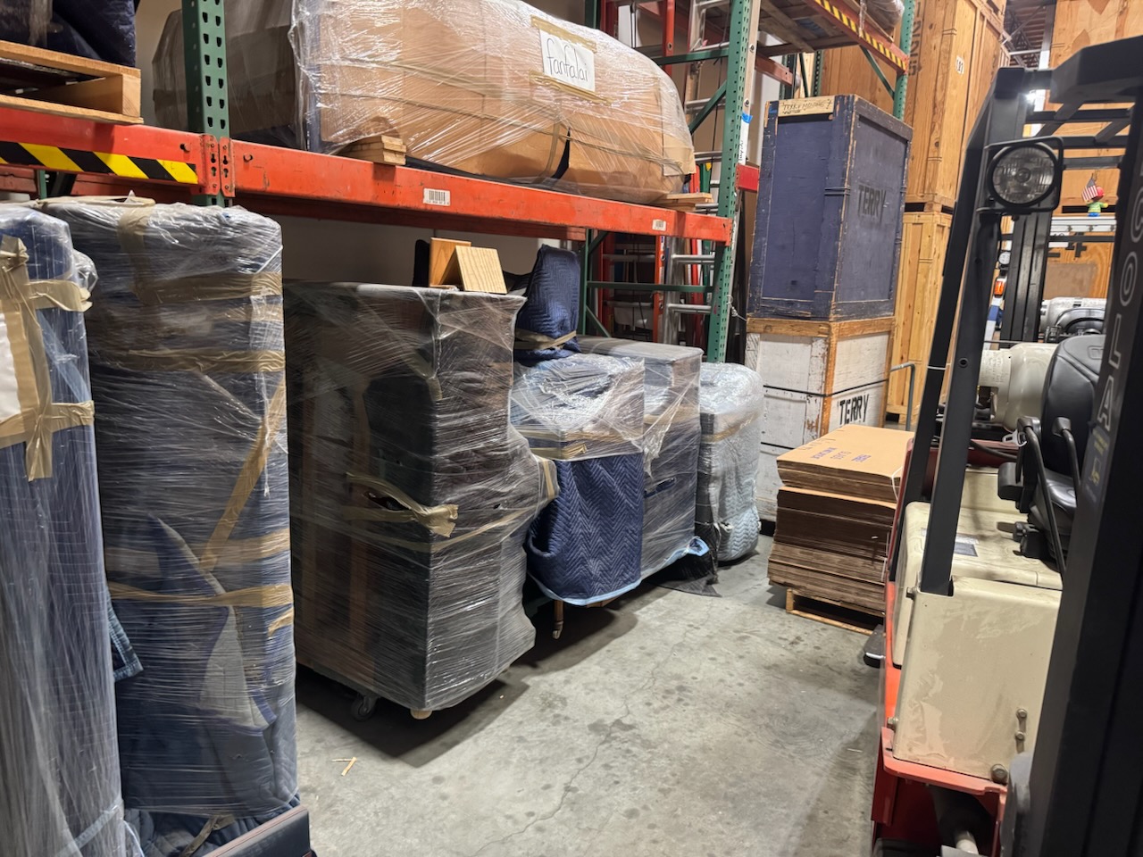 Storage area containing wrapped items, including pianos and furniture, on shelves and pallets. Storage area containing wrapped items, including pianos and furniture, on shelves and pallets.