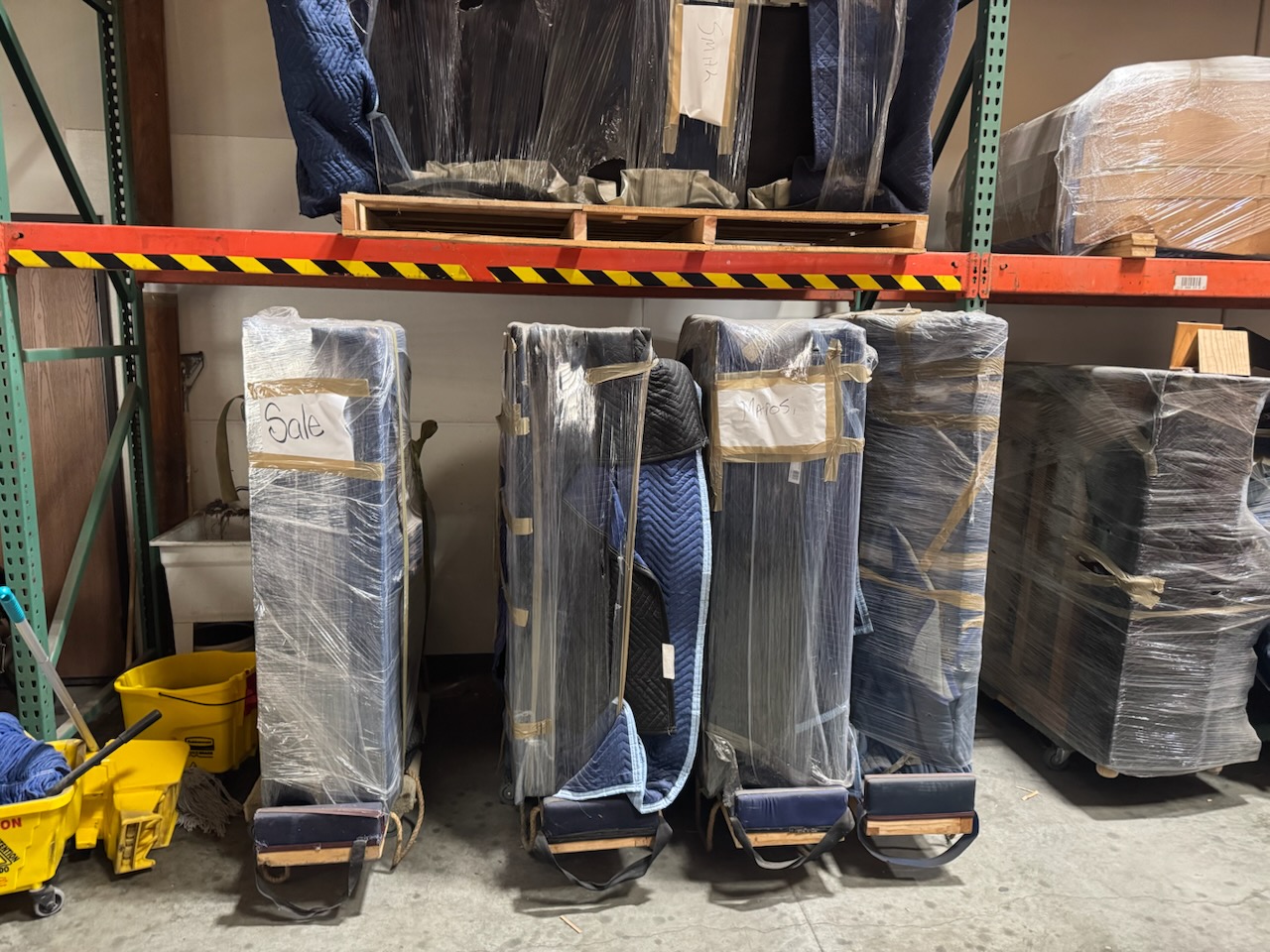 Terry-Moving-Pianos-Stored Storage area containing wrapped items, including pianos and furniture, on shelves and pallets.