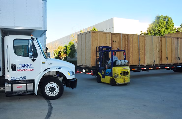 Forklift loading wooden crates onto a Terry Moving & Storage truck outside a warehouse.