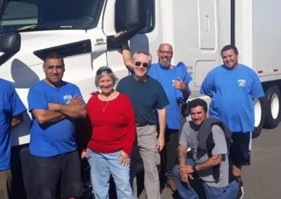 Group of movers in blue shirts posing with a smiling couple in front of a large white moving truck.