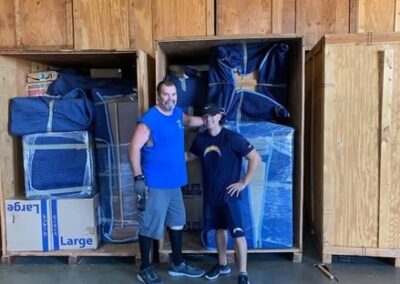 Two movers standing in front of large wooden storage crates filled with wrapped furniture and boxes.