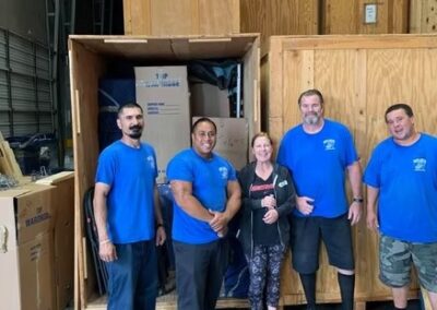 Five people, including four Terry Moving & Storage team members and a smiling customer, standing in front of open wooden storage crates inside a warehouse.