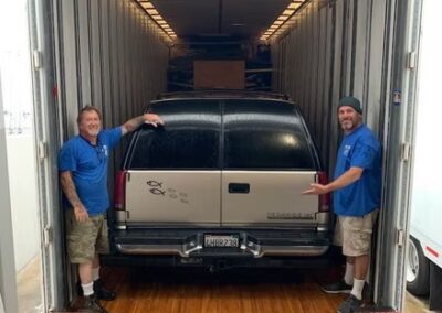 Two movers standing proudly beside a large SUV securely loaded inside a Terry Moving & Storage enclosed trailer.