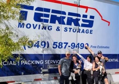 Happy family posing with their dogs in front of a Terry Moving & Storage truck on a sunny day.