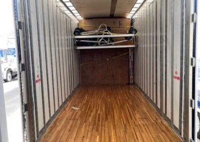 Interior of an empty moving trailer with polished wood flooring and equipment secured above.