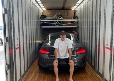 Man sitting on the back of a sports car inside a Terry Moving enclosed trailer, ready for transport.