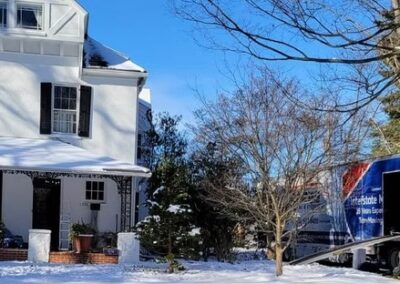 A moving truck parked in front of a house in a snowy residential area during winter.