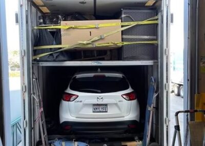 A white Mazda SUV parked inside a moving truck with cargo secured above it.