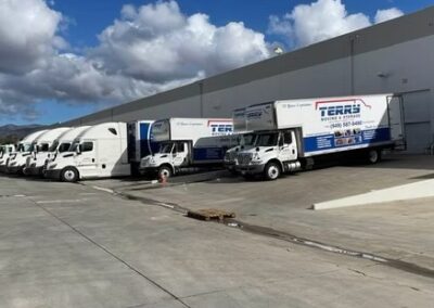 Multiple delivery trucks parked at a loading dock with a clear sky in the background.