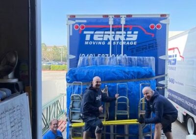 Three men posing in front of a moving truck filled with blue blankets and equipment.