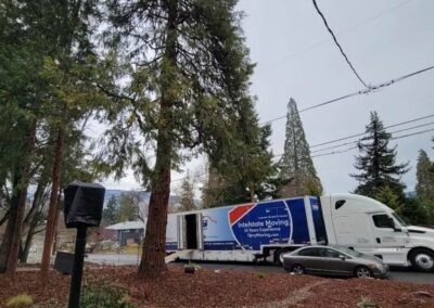 Large moving truck parked on a residential street surrounded by trees and parked cars.