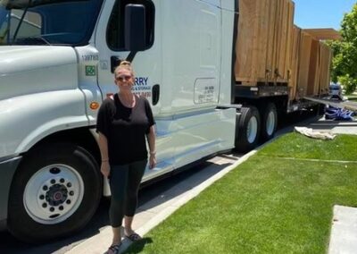 Woman standing next to a Terry Moving & Storage truck loaded with large wooden crates on a sunny day.