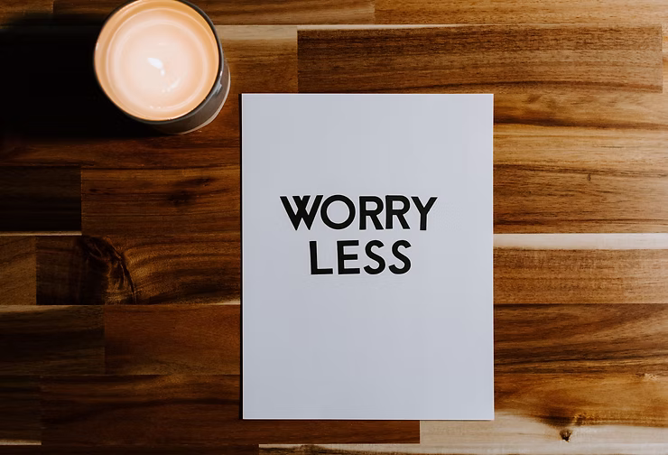 Minimalist card with the words “Worry Less” placed on a wooden table beside a lit candle.
